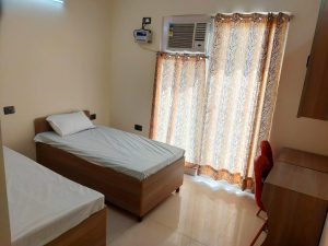 A picture of bedroom with bed, pillow, air condition, curtains, study table and chair